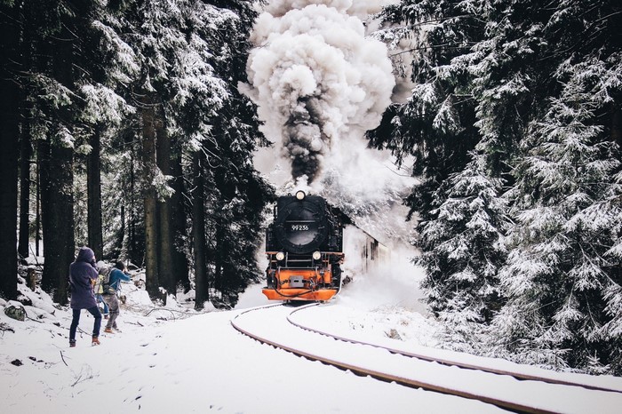 Steam train in a snowy forest with people