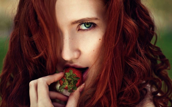 Close-up portrait of a redhead woman eating a strawberry