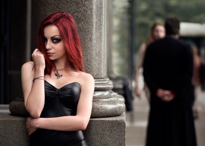 Woman with red hair in a black dress posing by a pillar