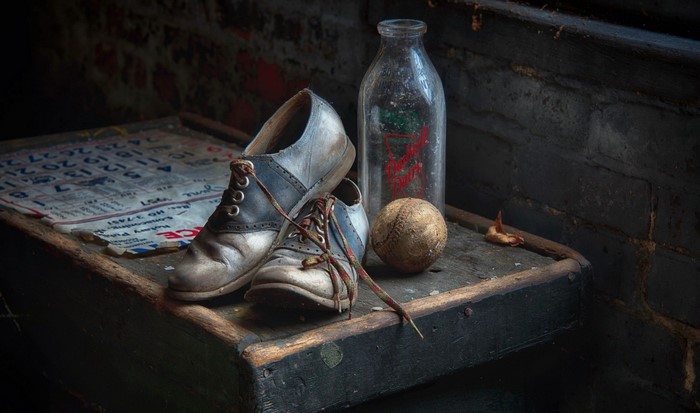 Old saddle shoes, baseball, and milk bottle on a table