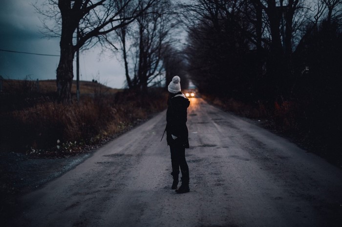 Woman in winter coat on a dark road at dusk