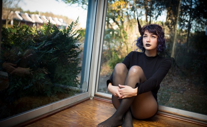 Woman with purple hair and horns sitting by a window