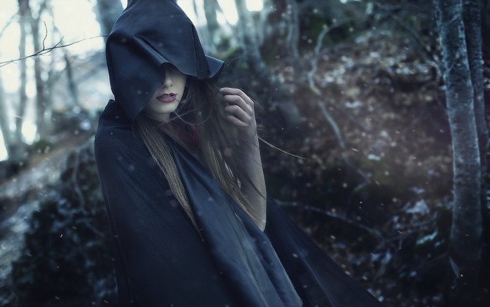 Woman in a black hood in a gloomy forest