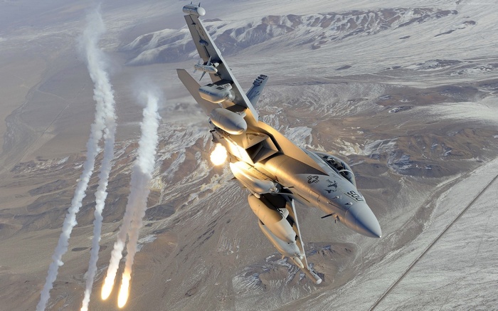 Boeing EA-18 Growler releasing flares over desert landscape