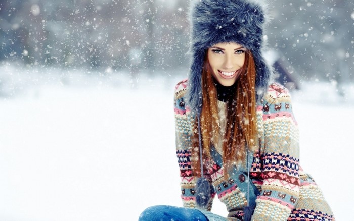 Woman with red hair wearing a fluffy hat and patterned sweater in snow