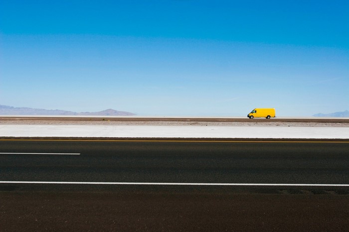Yellow van on a salt flat highway under a clear blue sky