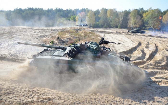 Tanks in a sandy training ground with trees in the background