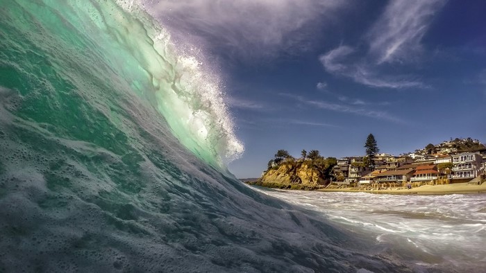 Wave crashing near Victoria Beach with houses on cliff
