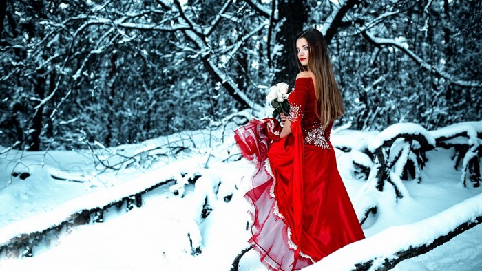 Woman in red dress holding white flowers in snowy forest