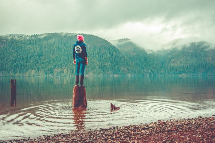 Woman standing on a log in a lake with mountains