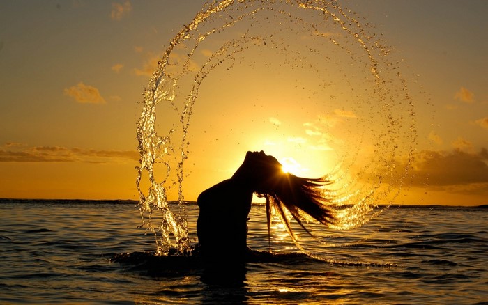 Woman splashing water at sunset in the ocean