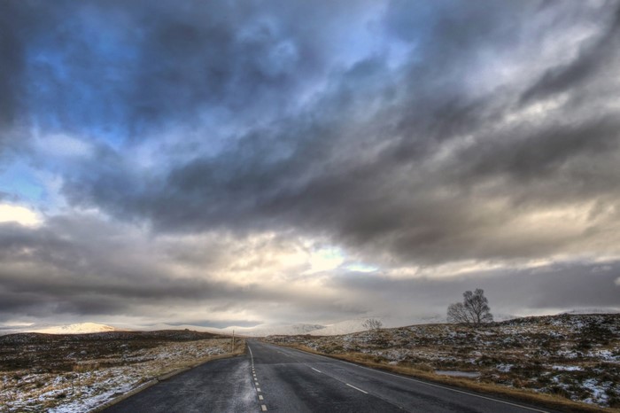 Road through snowy Scottish landscape under cloudy sky