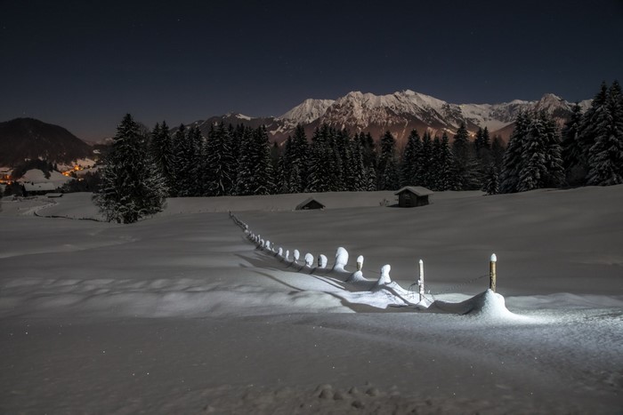 Snowy mountain landscape at night with a fence