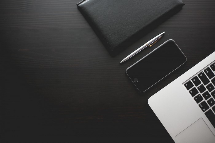 Laptop, smartphone, pen, and notebook on a dark wooden desk