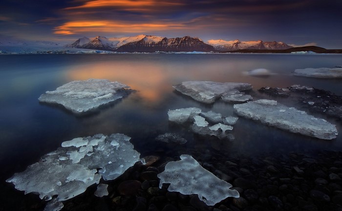 Icebergs floating in a lake with mountains at sunset