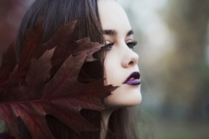 Woman with dark lipstick and leaf covering face