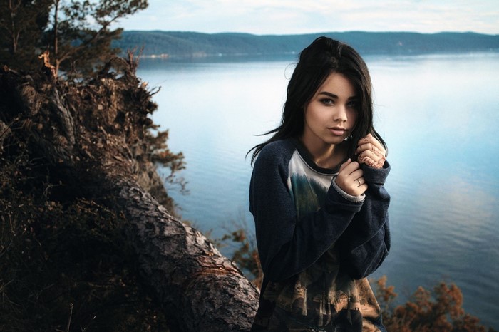 Woman posing by a lake with trees