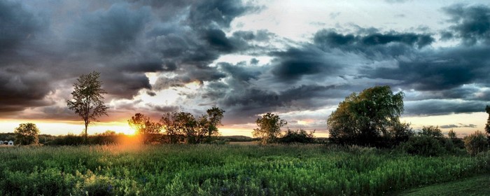 Sunset over a grassy field with dramatic clouds