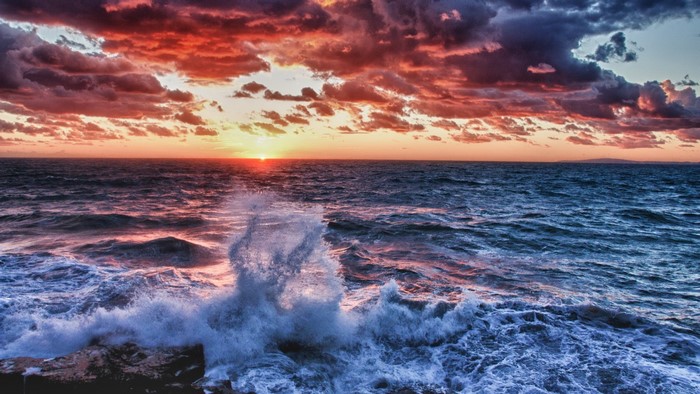 Dramatic Sunset Over Waves Crashing on Rocky Shore