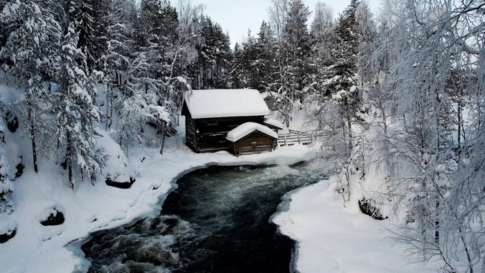 Wooden cabin by a river in a snowy forest