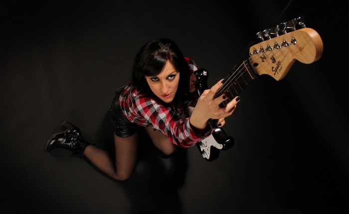Woman in plaid shirt and leather shorts holding a guitar