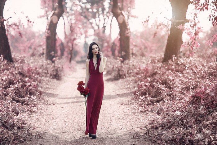 Woman in a red dress holding roses in a pink forest