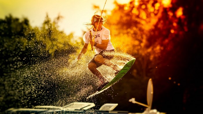Wakeboarder jumping with water splashes in sunlight