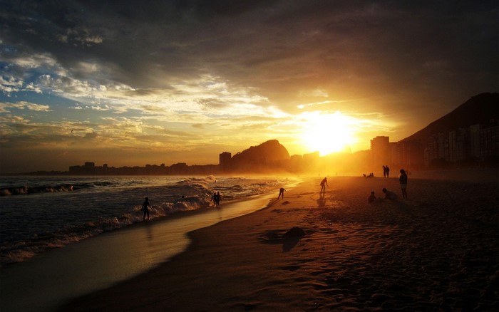 Sunset over a beach with people and city skyline