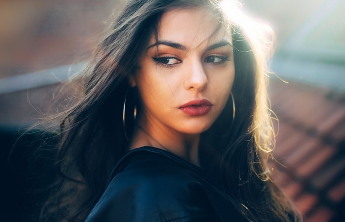 Woman with long brown hair and hoop earrings looking away