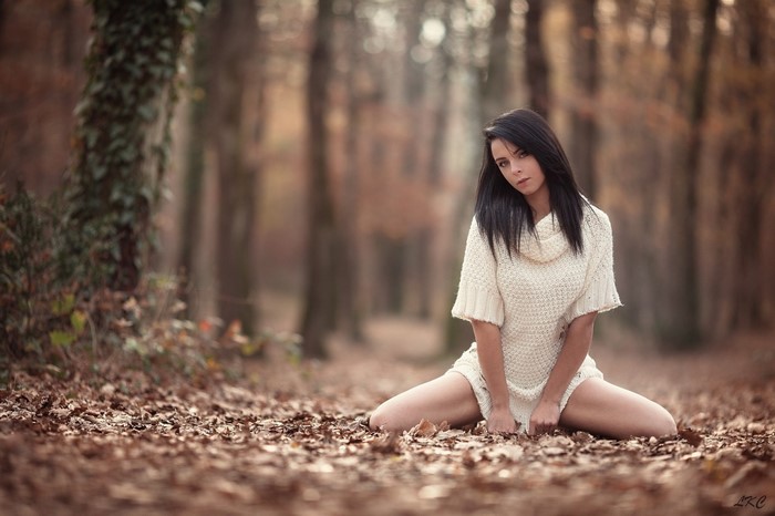 Woman in sweater dress sitting in autumn forest