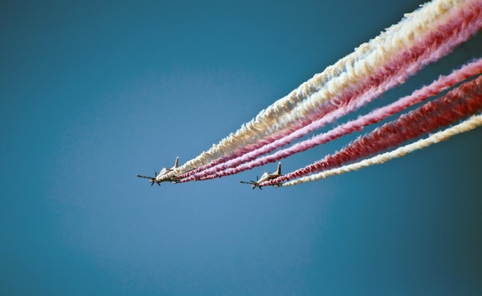 Two PZL 130 Orlik aircraft performing an airshow with red and white contrails