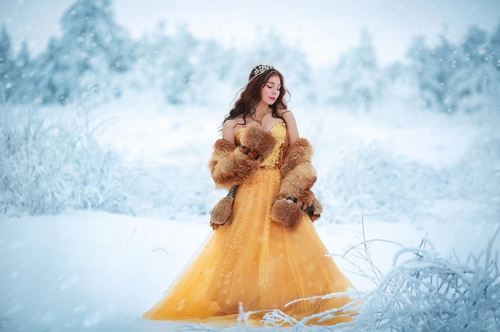 Woman in yellow dress and fur coat in snow