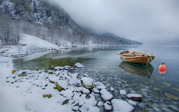 Wooden boat on a calm lake in winter with snow-covered mountains