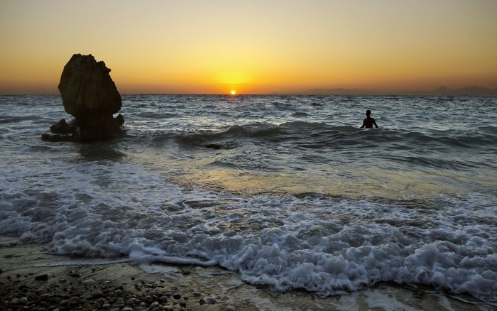 Person swimming in the sea at sunset with rock formation