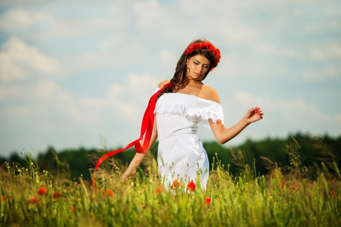 Woman in white dress with red flower crown in a field