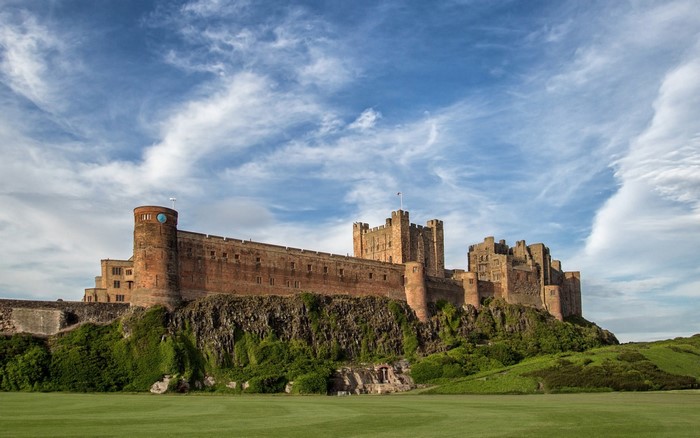Bamburgh Castle on a grassy hill under a cloudy sky