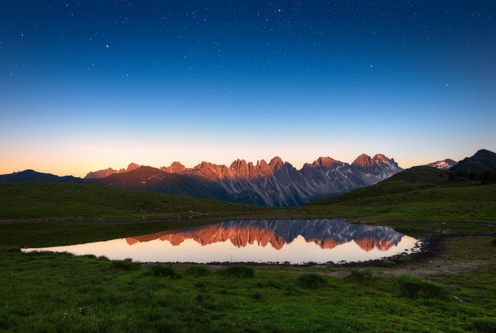 Mountain range reflected in a lake at dusk with stars