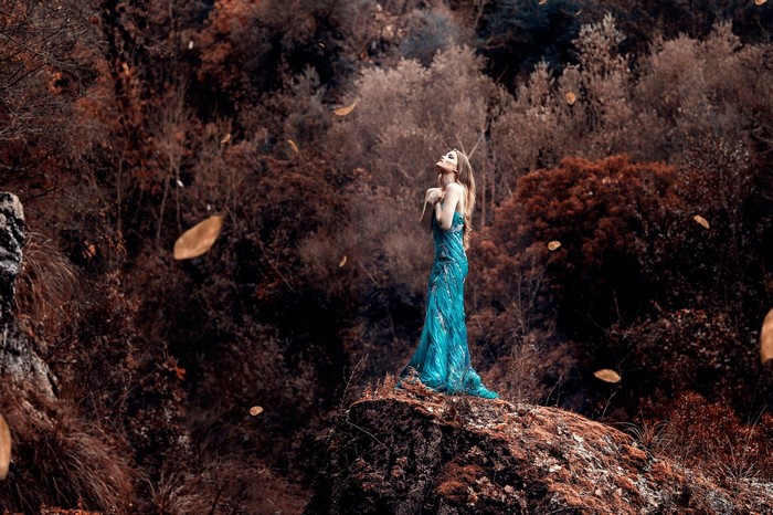 Woman in blue dress standing on a rock in autumn forest