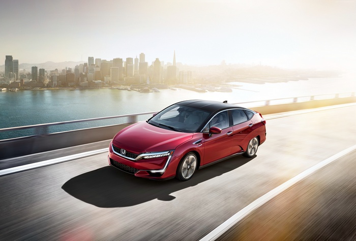 Red Honda Clarity EV driving on a bridge with city skyline