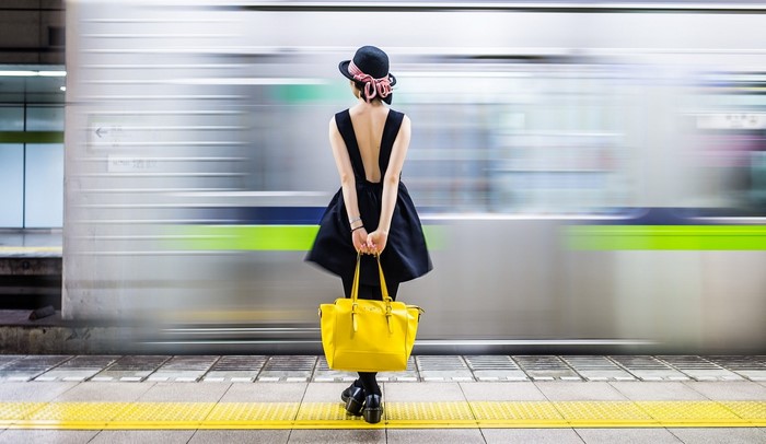 Woman in black dress and hat with yellow bag at train station