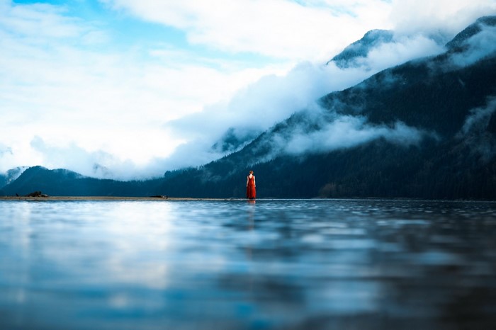 Woman in red dress by misty mountains and lake