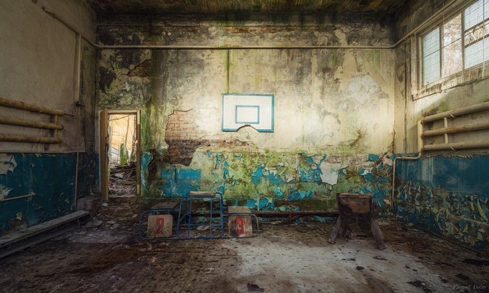 Abandoned gymnasium with basketball hoop and decaying walls