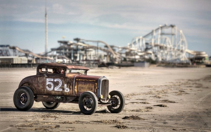 Rusty hot rod car with number 52 on a beach with roller coaster