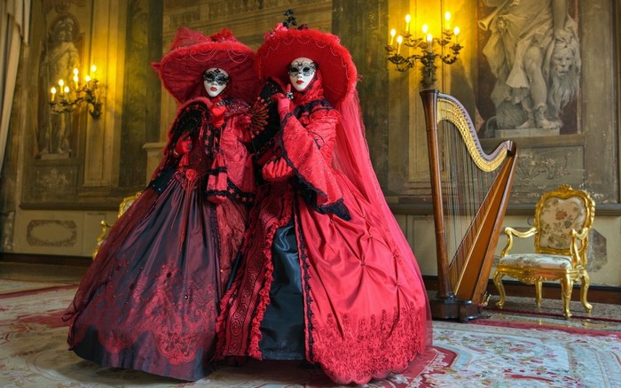 Two women in red Venetian carnival costumes with masks and a harp