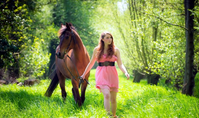 Woman walking with a horse in a green forest