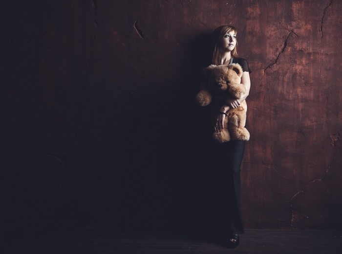 Woman holding a teddy bear against a textured wall