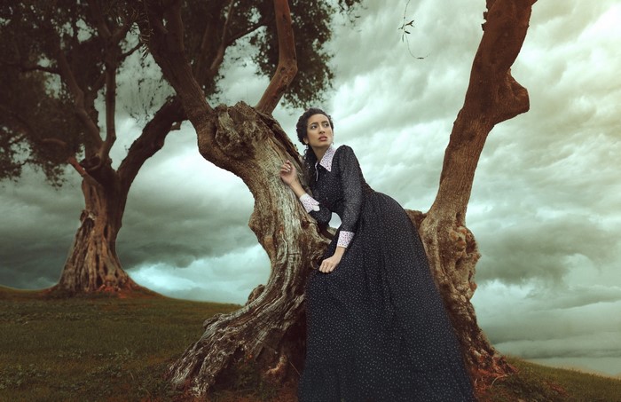 Woman in a dark dress leaning against a tree
