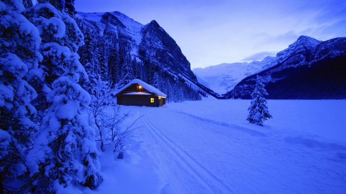 Winter cabin in snowy mountain landscape at dusk