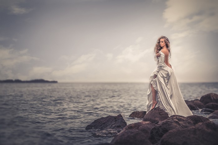 Woman in a white dress on rocks by the sea