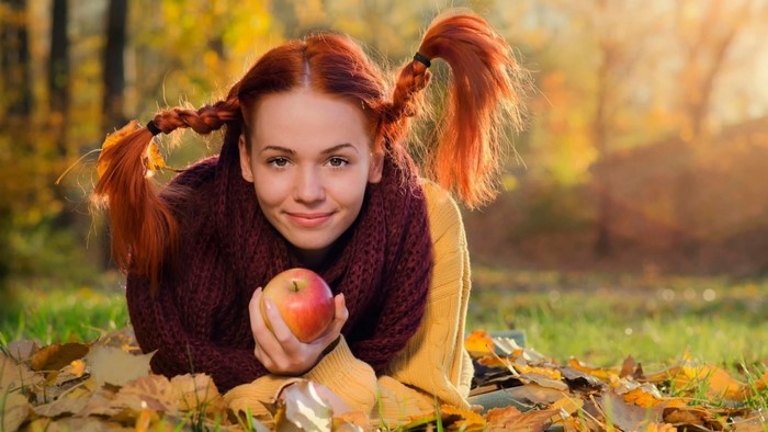Redhead girl with braids holding an apple in autumn